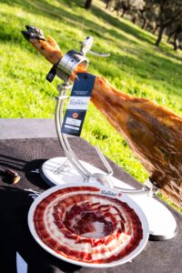 Jamón ibérico de bellota DOP Los Pedroches en jamonero con plato de lonchas en dehesa